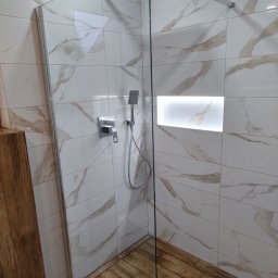 Barthouse Bartosz Waksmundzki - Kabina prysznicowa z deszczownicą i wnęką z podświetleniem, wykończona płytkami imitującymi marmur i drewno. Nowoczesny design.