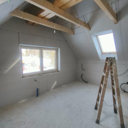 Barthouse Bartosz Waksmundzki - Poddasze w trakcie adaptacji: ściany obłożone płytami gips-karton, widoczne drewniane belki stropowe, okno dachowe i drabina. Prace wykończeniowe.
