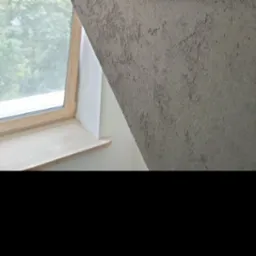 Szara ściana ze strukturą przy oknie dachowym z drewnianą ramą i parapetem, widok z dołu, blisko okna, nierówna faktura.