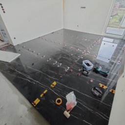 Barthouse Bartosz Waksmundzki - Układanie czarnych płytek z białym wzorem w Łopusznej. Widoczne narzędzia glazurnicze i system poziomowania. Podłoga w trakcie realizacji.