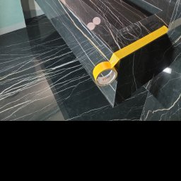 Barthouse Bartosz Waksmundzki - Czarny marmur z białymi żyłkami, zabezpieczony żółtą taśmą malarską w rogu, na podłodze z tego samego materiału. Ochrona przed zabrudzeniem podczas prac.