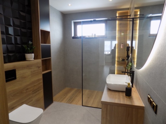 Nowoczesna łazienka z kabiną typu walk-in, umywalką nablatową i czarną ścianą z geometrycznym wzorem. Drewniane akcenty i oświetlenie LED.