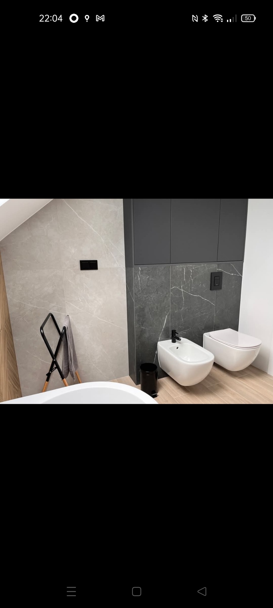 Elegancka łazienka z marmurowymi płytkami, wiszącą toaletą i bidetem. Czarne akcenty armatury i dodatków. Minimalistyczny design i nowoczesne wykończenie.