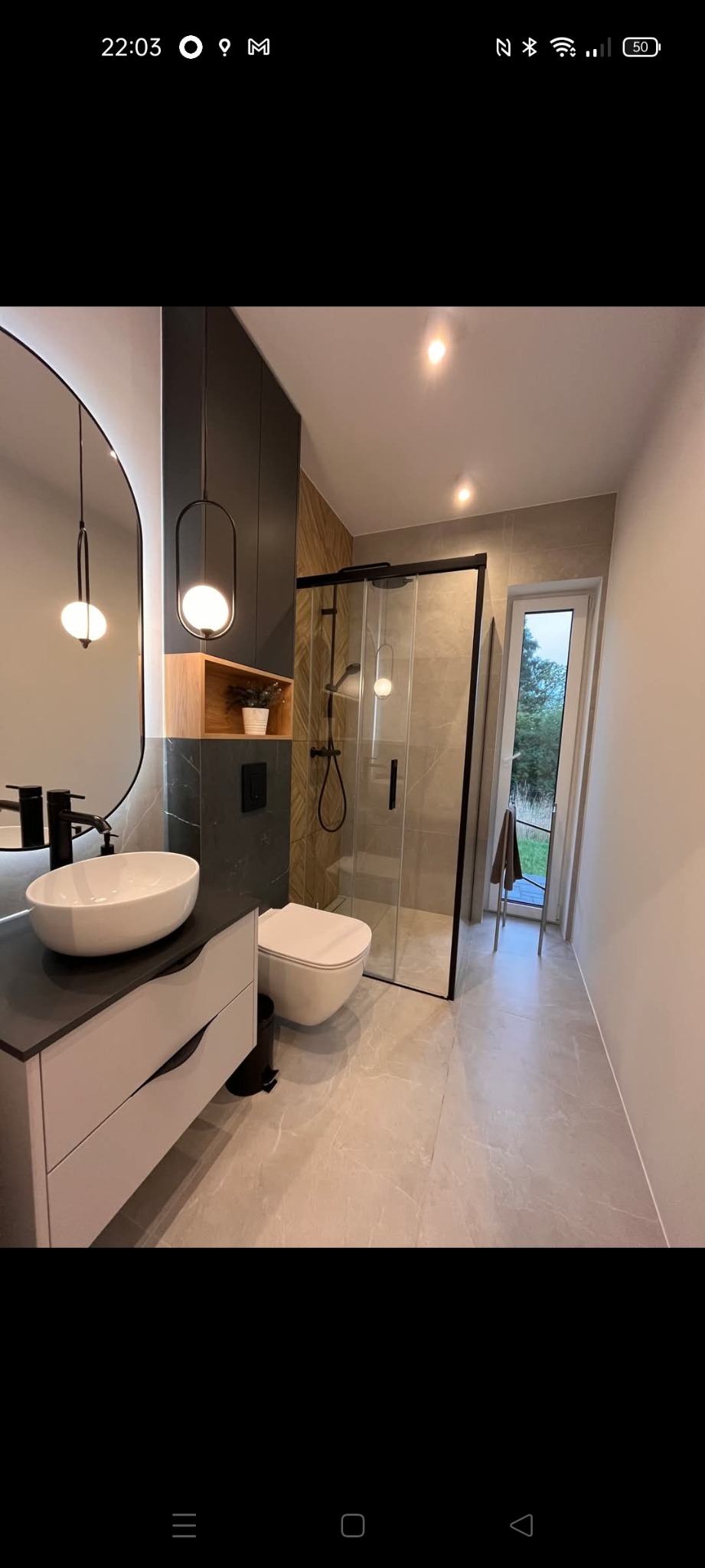 Nowoczesna łazienka z kabiną prysznicową typu walk-in, umywalką nablatową i szafką pod umywalką w odcieniach szarości, oświetlona lampą wiszącą.