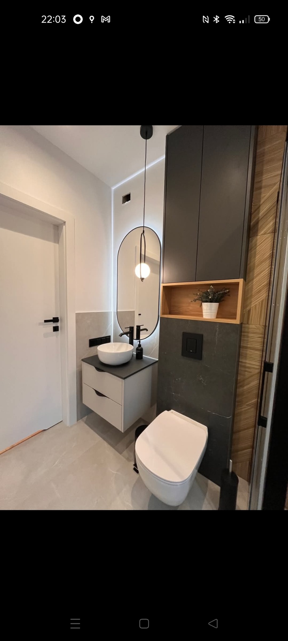 Nowoczesna łazienka z podwieszaną toaletą, umywalką nablatową i lustrem z podświetleniem LED. Drewniane akcenty i szara armatura tworzą elegancki design.