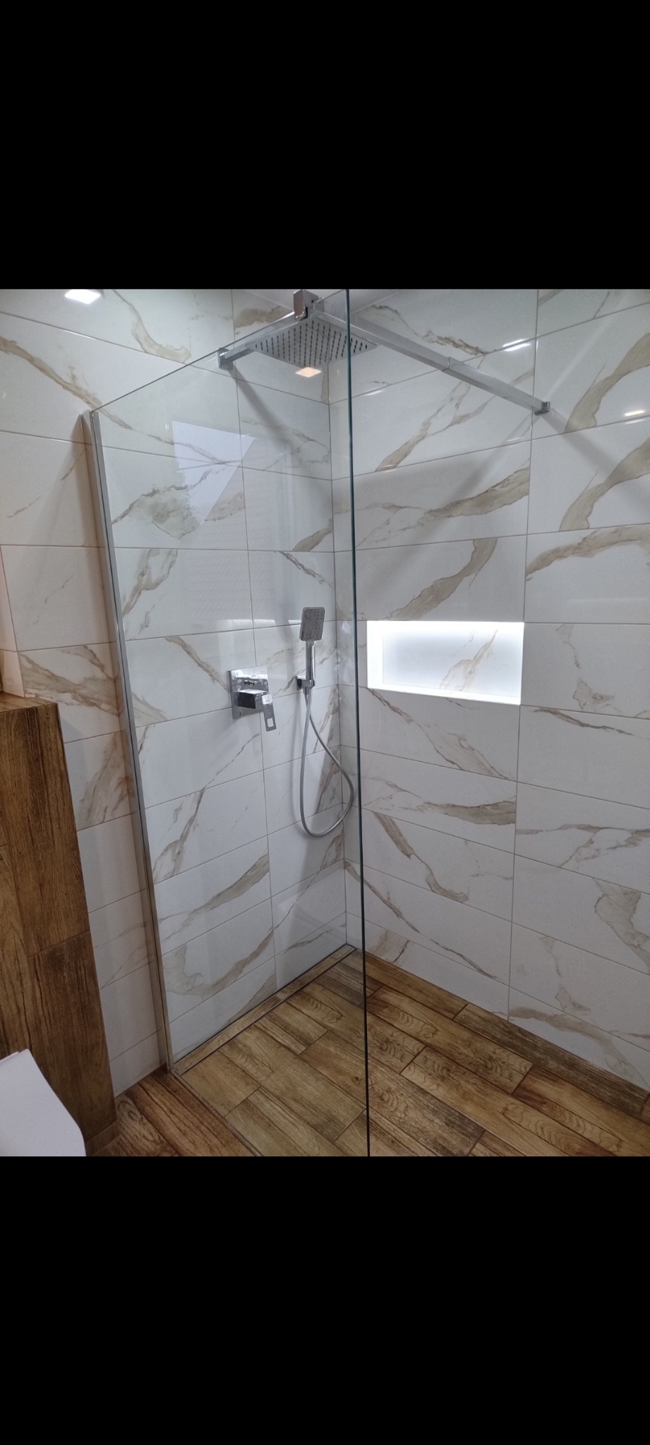 Kabina prysznicowa z deszczownicą i wnęką z podświetleniem, wykończona płytkami imitującymi marmur i drewno. Nowoczesny design.