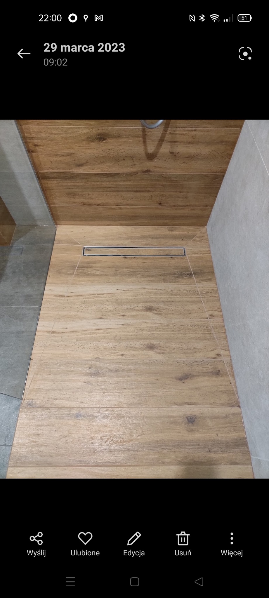 Ukończona kabina prysznicowa z drewnopodobnymi płytkami i odpływem liniowym. Jasne płytki na ścianach. Widok z góry, wnętrze łazienki.