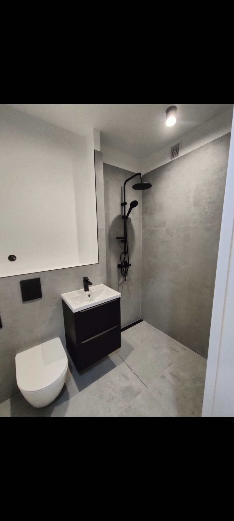 Nowoczesna łazienka w szarościach z czarną armaturą: kabina prysznicowa typu walk-in, umywalka z szafką i toaleta. Minimalistyczny design, gładkie płytki.