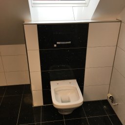 Mariusz Sienkiewicz - Nowoczesna toaleta podwieszana w łazience na poddaszu, z czarno-białymi płytkami z brokatem, widok na okno dachowe.