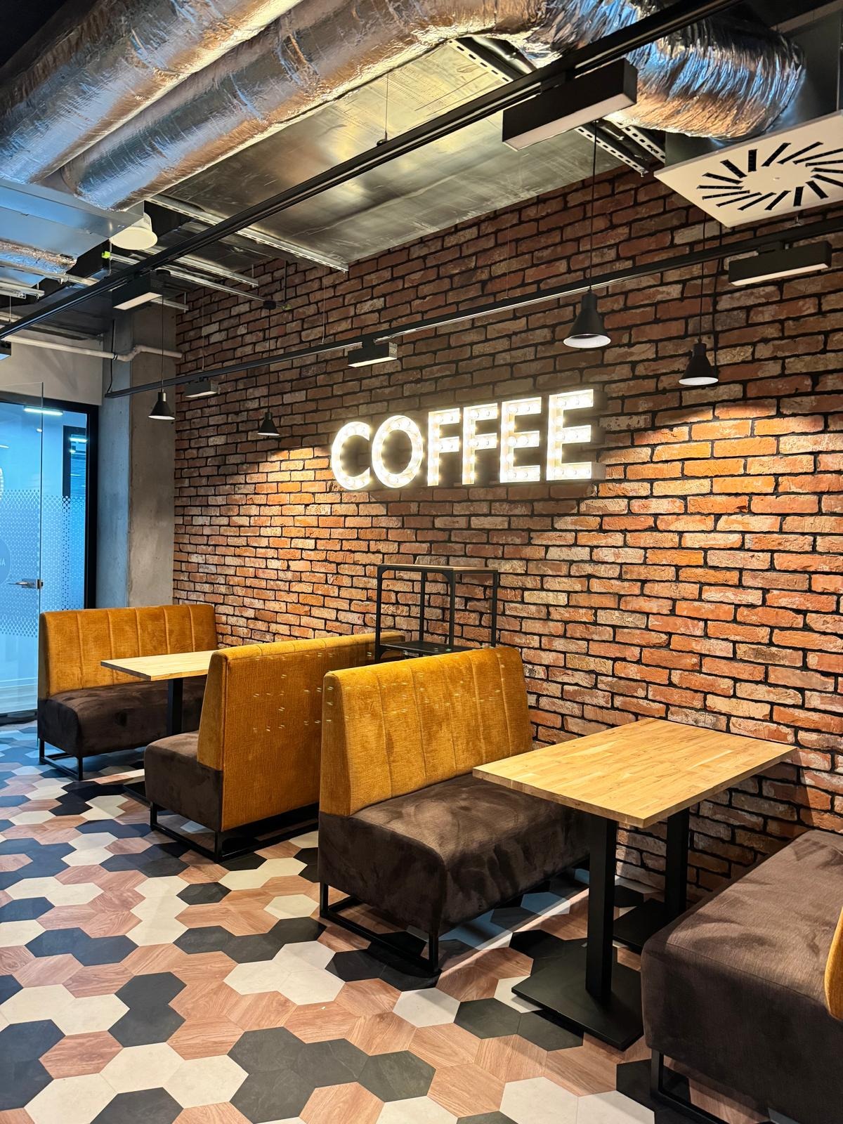 Stylowe wnętrze kawiarni w Warszawie z ceglaną ścianą, podświetlanym napisem 'COFFEE', żółtymi lożami i geometryczną podłogą.