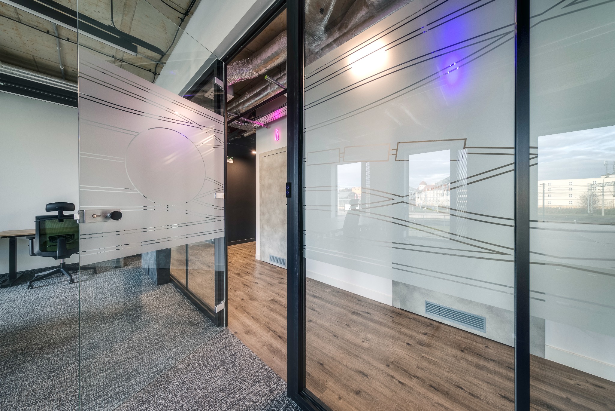 Nowoczesne biuro z przeszklonymi ścianami z dekoracyjnym matowym wzorem, widok na korytarz z oświetleniem LED i biurko z krzesłem.