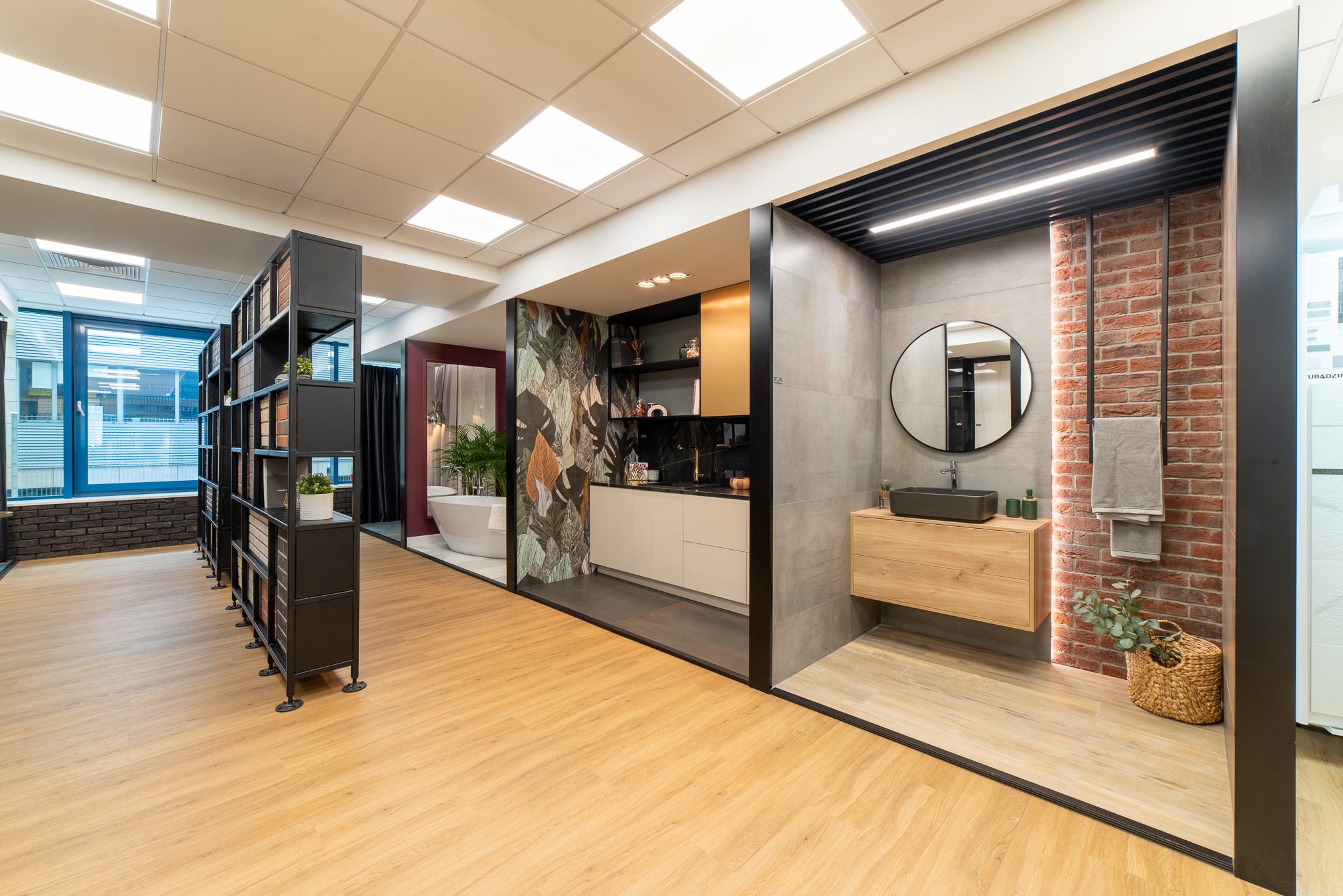 Wnętrze biura z ekspozycją aranżacji łazienek i kuchni, prezentujące różne style wykończenia, od nowoczesnego minimalizmu po rustykalny z elementami cegły i naturalnych materiałów.