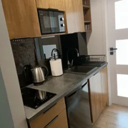 Nowoczesna kuchnia z drewnianymi szafkami, czarnym blatem, płytą indukcyjną i wbudowaną mikrofal&oacute;wką Sharp.