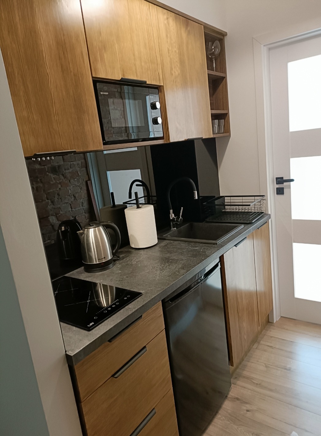 Nowoczesna kuchnia z drewnianymi szafkami, czarnym blatem, płytą indukcyjną i wbudowaną mikrofalówką Sharp.