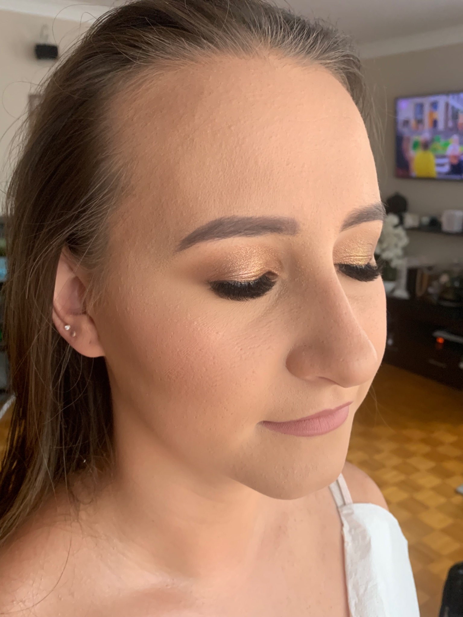 Profil młodej kobiety z zamkniętymi oczami, prezentujący złoty makijaż oczu z wyraźnie podkreślonymi rzęsami i delikatnie różowe usta.