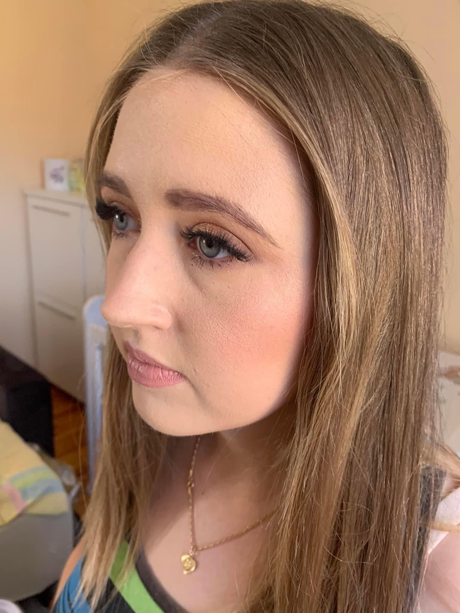 Portret profilowy kobiety z delikatnym, naturalnym makijażem oczu w odcieniach złota i brązu, podkreślonymi rzęsami oraz subtelnym różem na policzkach, na tle jasnego wnętrza.