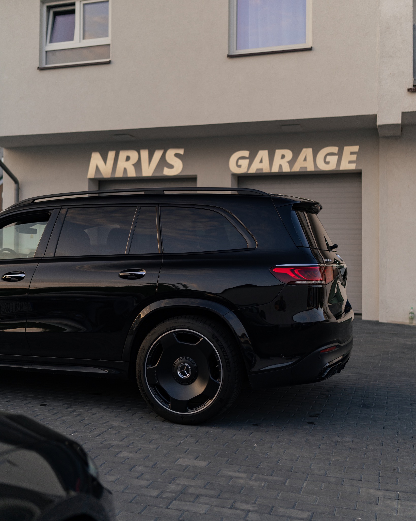 Czarny Mercedes GLS 63 AMG zaparkowany przed garażem NRVS Garage, widok z tyłu, z widocznymi detalami felg i lamp.