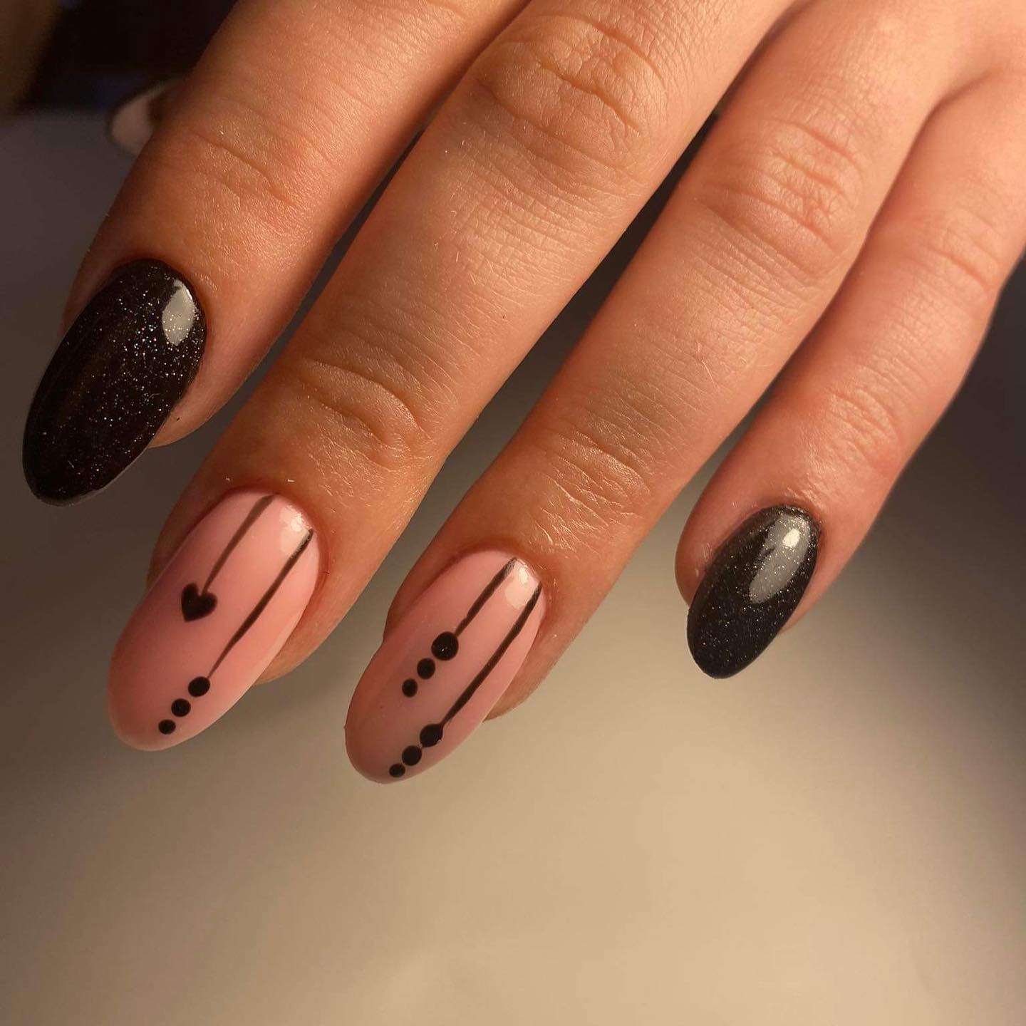 Dłoń z owalnymi paznokciami: dwa w kolorze czarnym ze srebrnym brokatem, dwa w kolorze pudrowego różu z czarnymi liniami i kropkami, jeden z serduszkiem.