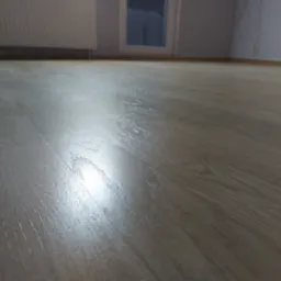 Jasna, lakierowana podłoga parkietowa w Gdyni, z widocznym odbiciem światła, na tle ściany i okna.