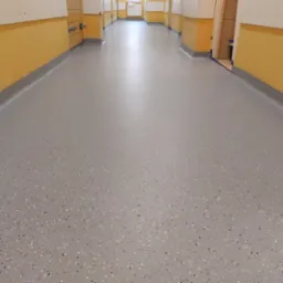 Korytarz z nową, szarą posadzką z kolorowymi chipsami, świeżo po wylaniu, z widocznymi żółtymi ścianami i szarymi listwami przypodłogowymi.