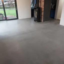 Szara, gładka posadzka we wnętrzu domu w Gdyni, z widocznym kominkiem i dużym oknem balkonowym wychodzącym na ogród.