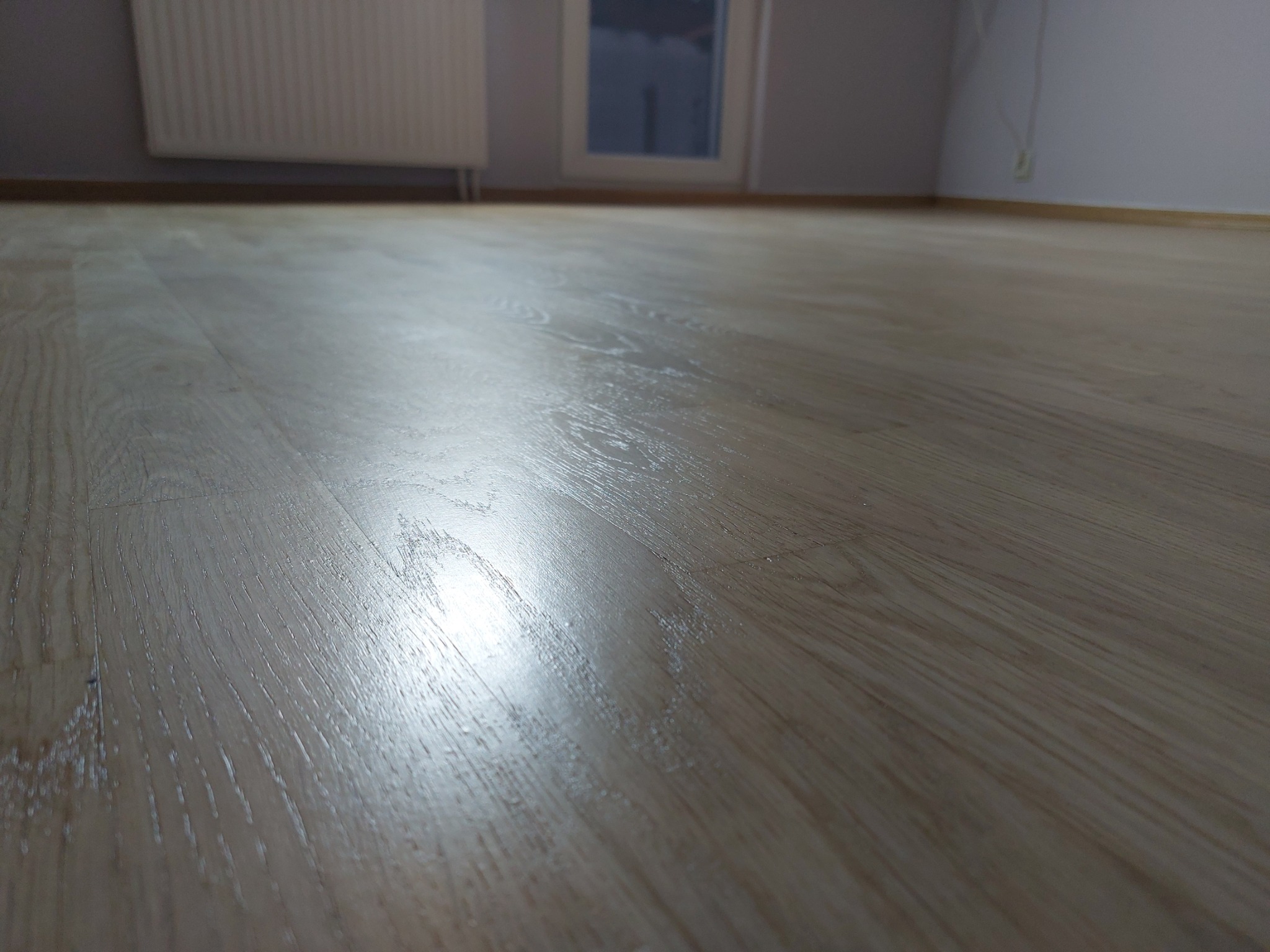 Jasna, lakierowana podłoga parkietowa w Gdyni, z widocznym odbiciem światła, na tle ściany i okna.