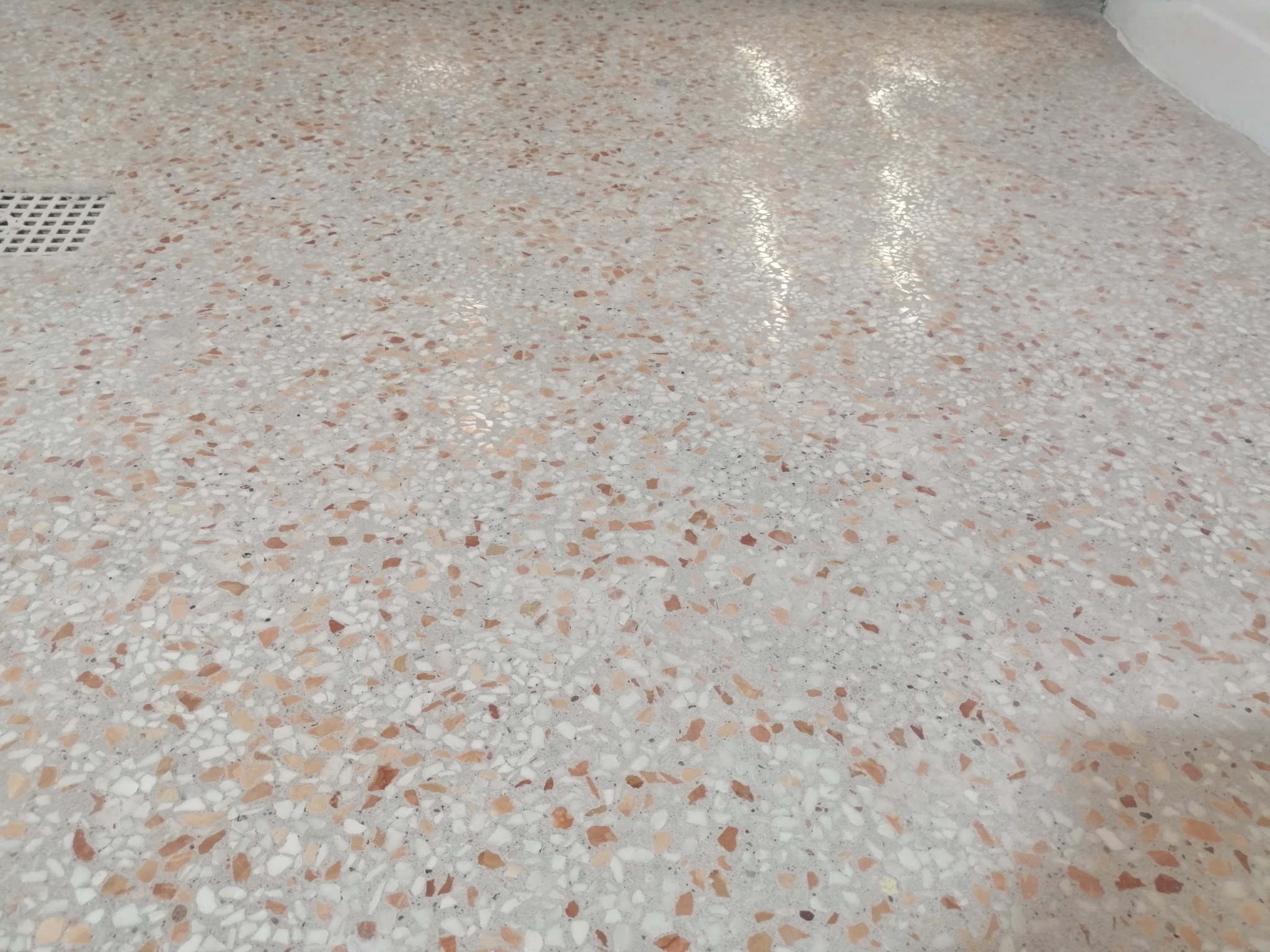 Polerowana posadzka lastryko w odcieniach szarości, bieli i brązu z widocznym odpływem podłogowym i refleksami światła.