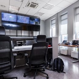 Marlena Grablowska - Jasne biuro z widocznymi stanowiskami pracy, monitorami prezentującymi schematy i planami architektonicznymi, kalendarzem na ścianie i elementami wyposażenia biurowego.