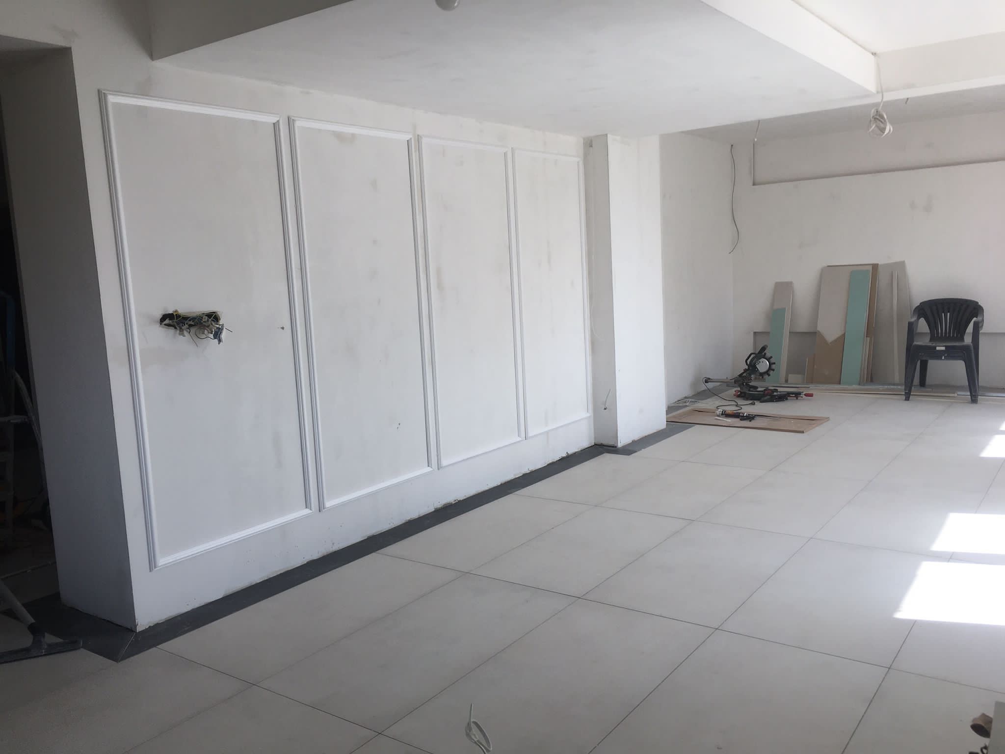 Wnętrze w trakcie prac wykończeniowych: ściany z dekoracyjnymi panelami, widoczne przewody elektryczne, narzędzia i płyty na podłodze.
