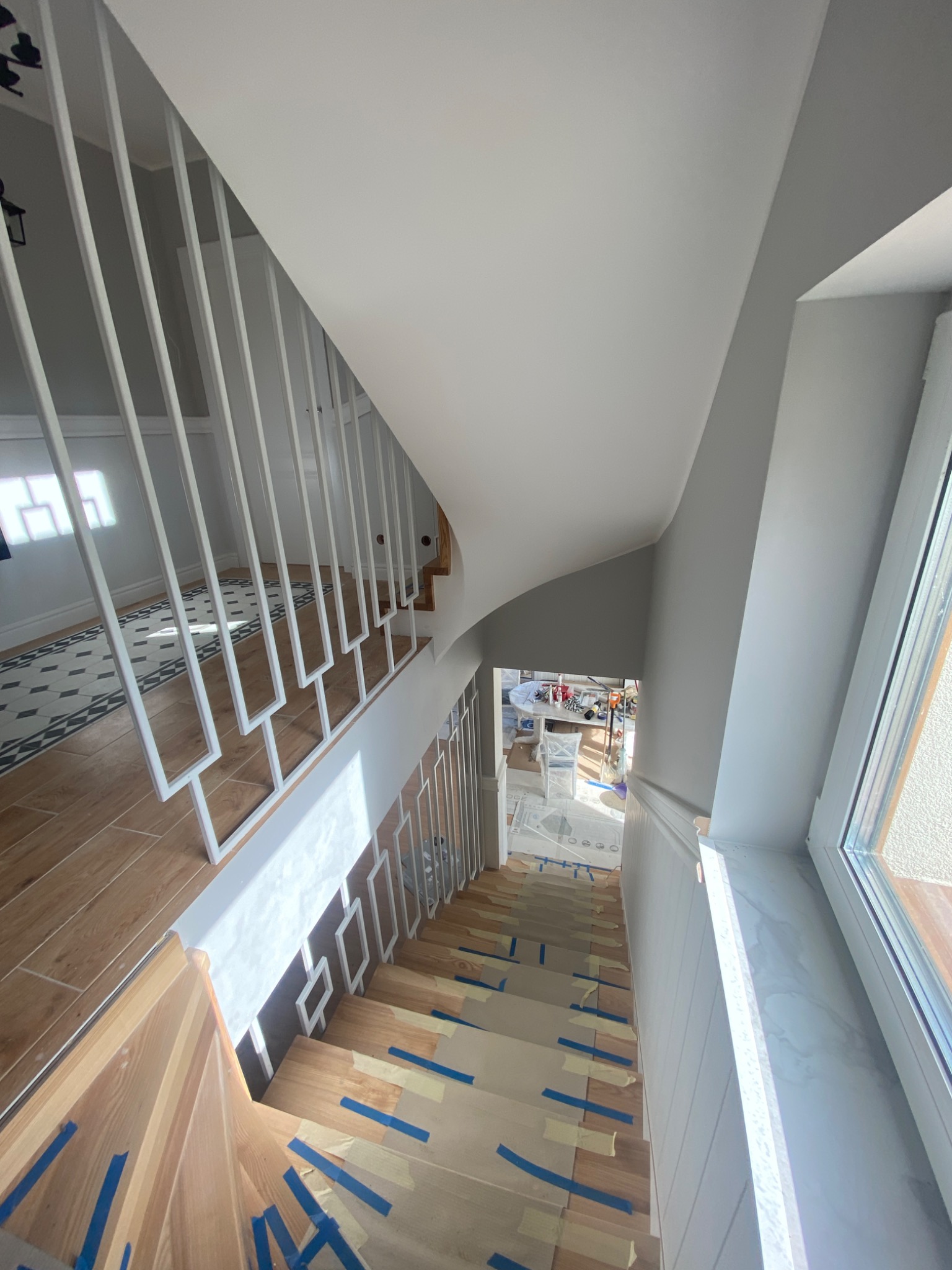 Schody drewniane z nowoczesną białą balustradą w trakcie zabezpieczania taśmą malarską przed pracami wykończeniowymi.