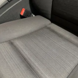 Ciemnoszara tapicerka samochodowa z widocznym zapięciem pasa bezpieczeństwa, prezentująca splot materiału i delikatne załamania światła.