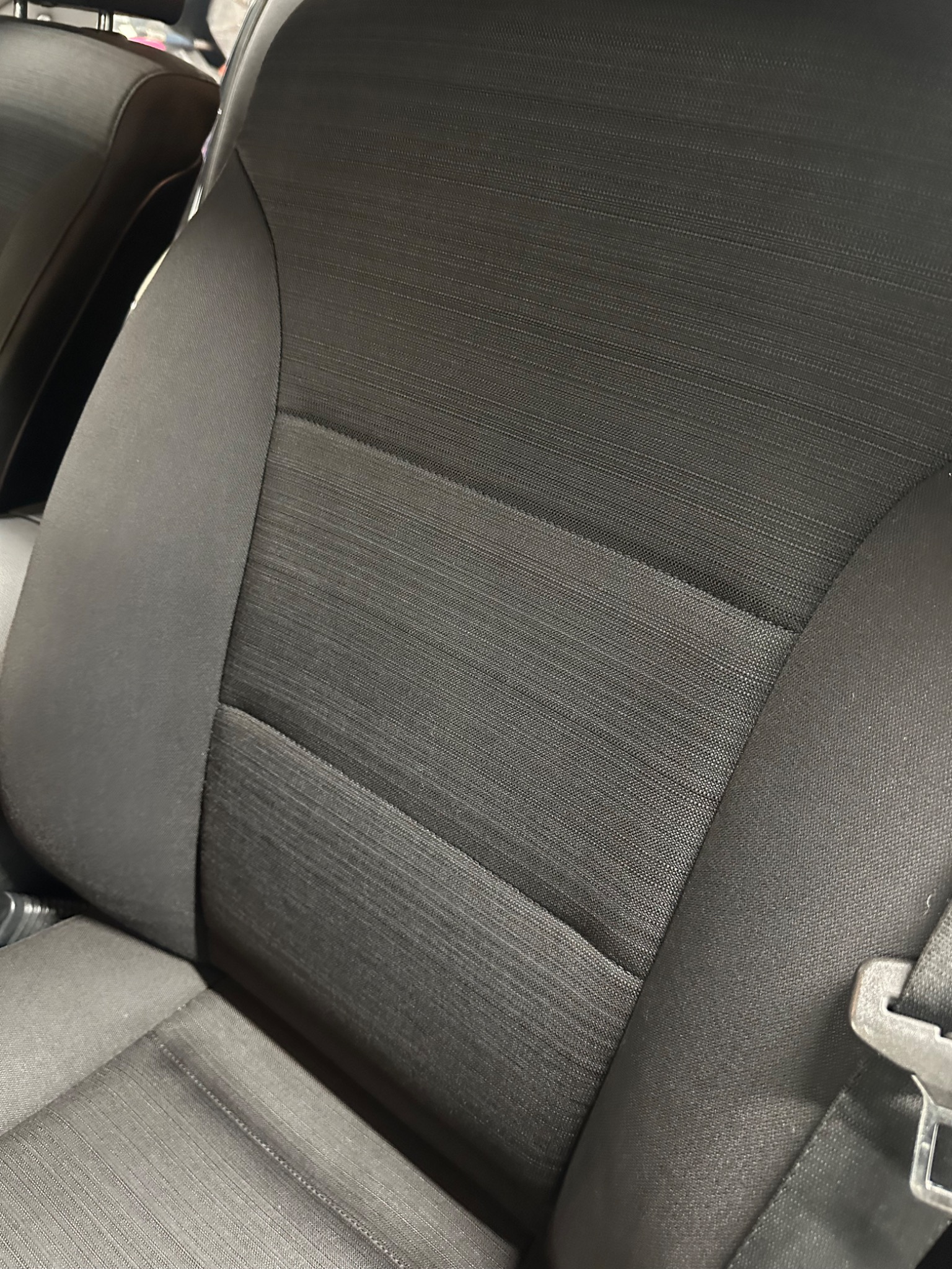 Ciemna, teksturowana tapicerka samochodowa z widocznym pasem bezpieczeństwa i fragmentem zagłówka.