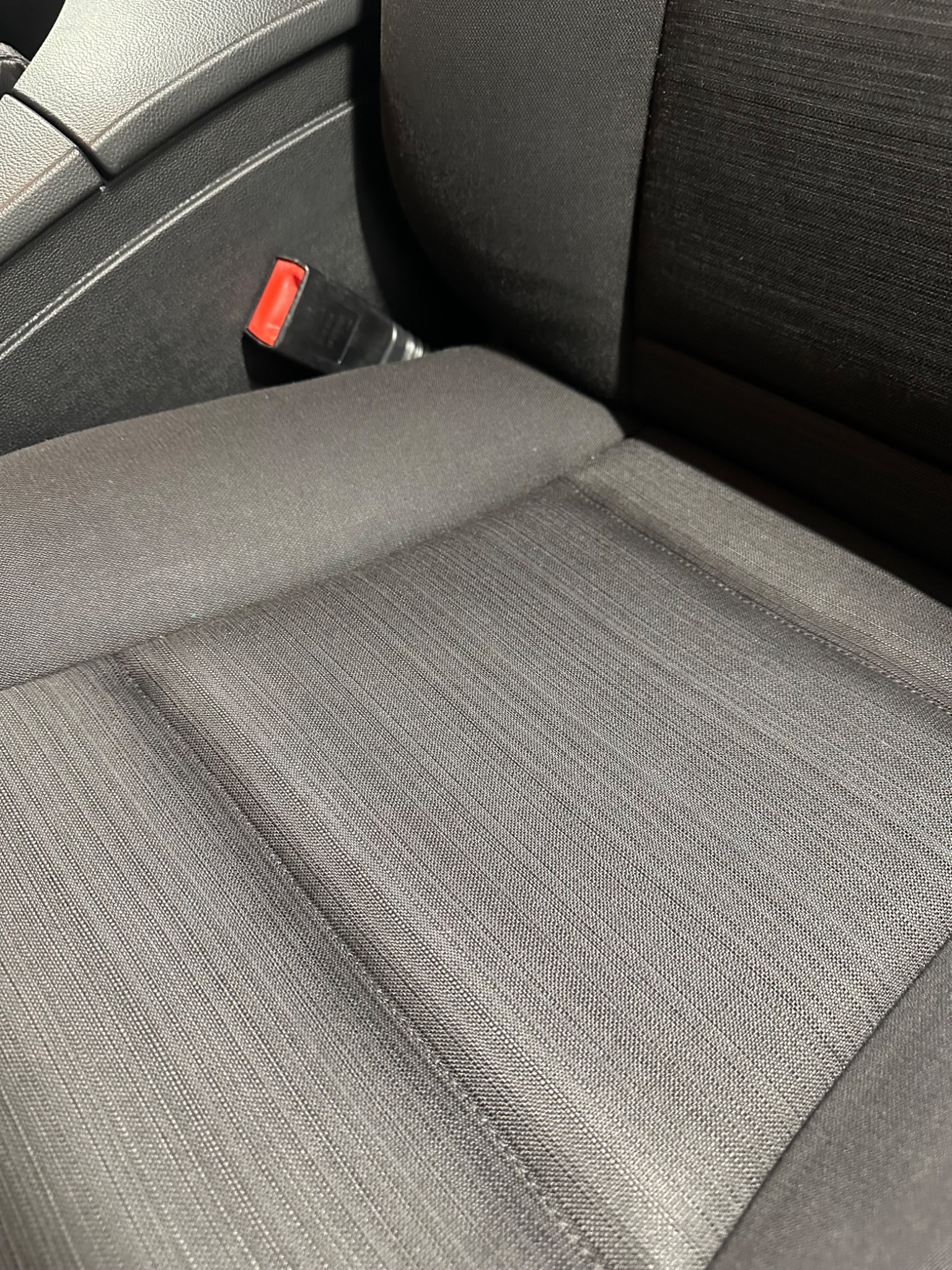 Ciemnoszara tapicerka samochodowa z widocznym zapięciem pasa bezpieczeństwa, prezentująca splot materiału i delikatne załamania światła.