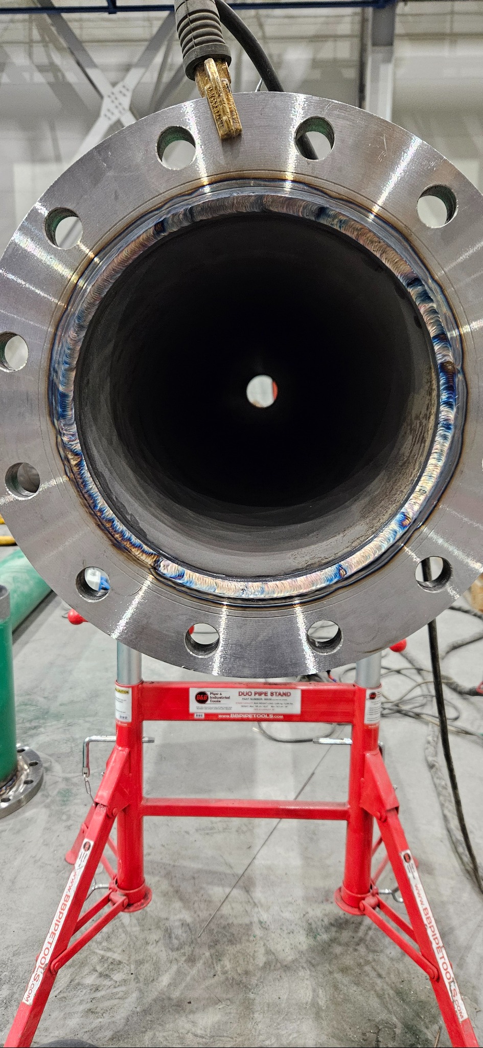 Wnętrze spawanej rury przemysłowej z kołnierzem, widoczne ślady spawania. Rura umieszczona na czerwonym stojaku. Widok z bliska, centralny kadr.