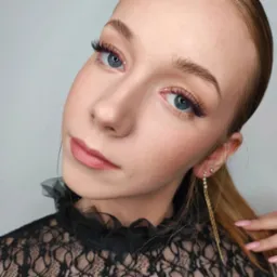 Portret młodej kobiety z delikatnym, różowym cieniem na powiekach, przedłużonymi rzęsami z fioletowymi akcentami, oraz subtelnie podkreślonymi ustami w kolorze nude, uzupełniony długimi, złotymi...