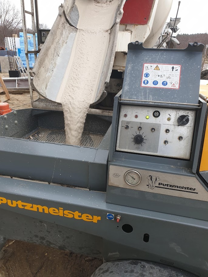 Anhydrytowa wylewka spływająca z betonomieszarki do pompy Putzmeister na budowie, widoczne elementy sterujące i wskaźniki pompy.