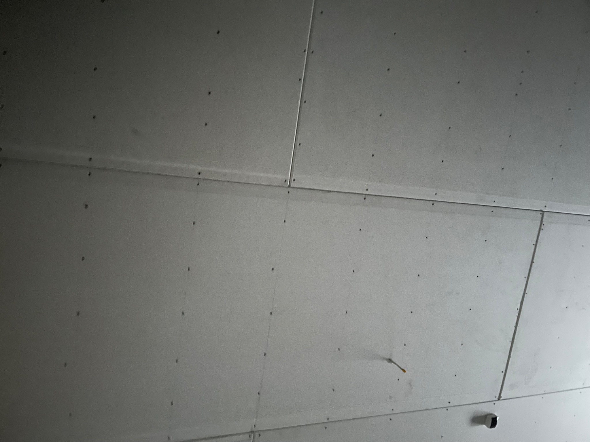 Płyty gipsowo-kartonowe zamontowane na suficie, widoczne łączenia i wkręty, w tle wystający przewód elektryczny.