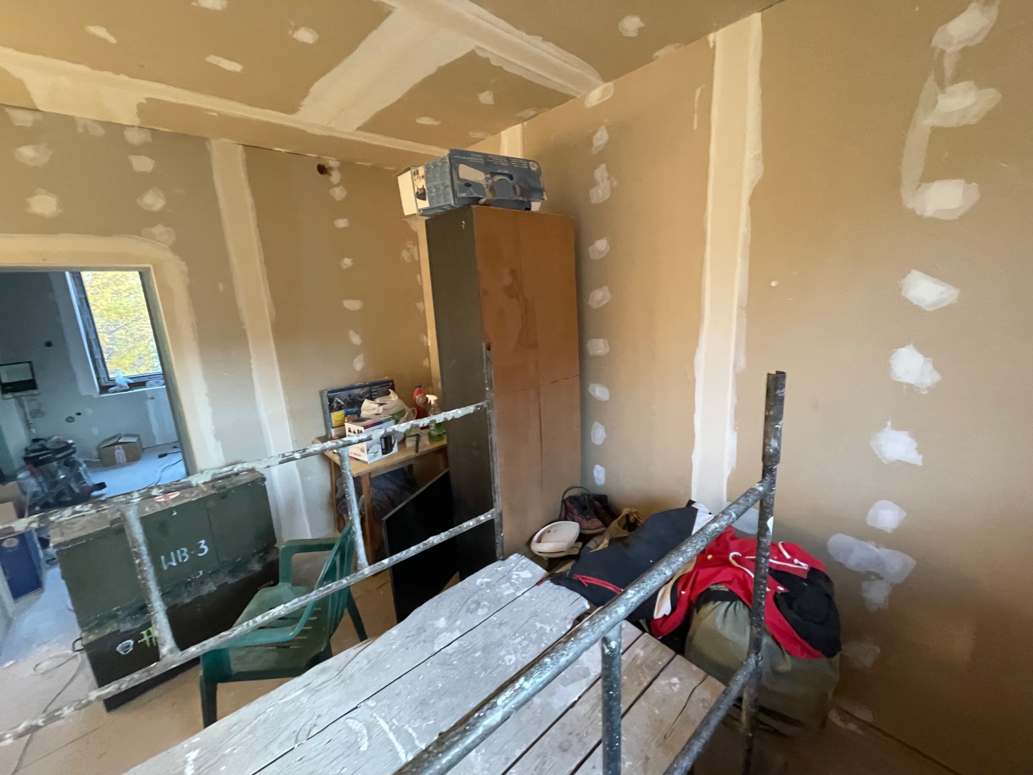 Wnętrze w trakcie prac w Lublinie: ściany przygotowane do dalszych prac, widoczne ślady po szpachlowaniu, rusztowanie, meble zabezpieczone, karton na szafie.