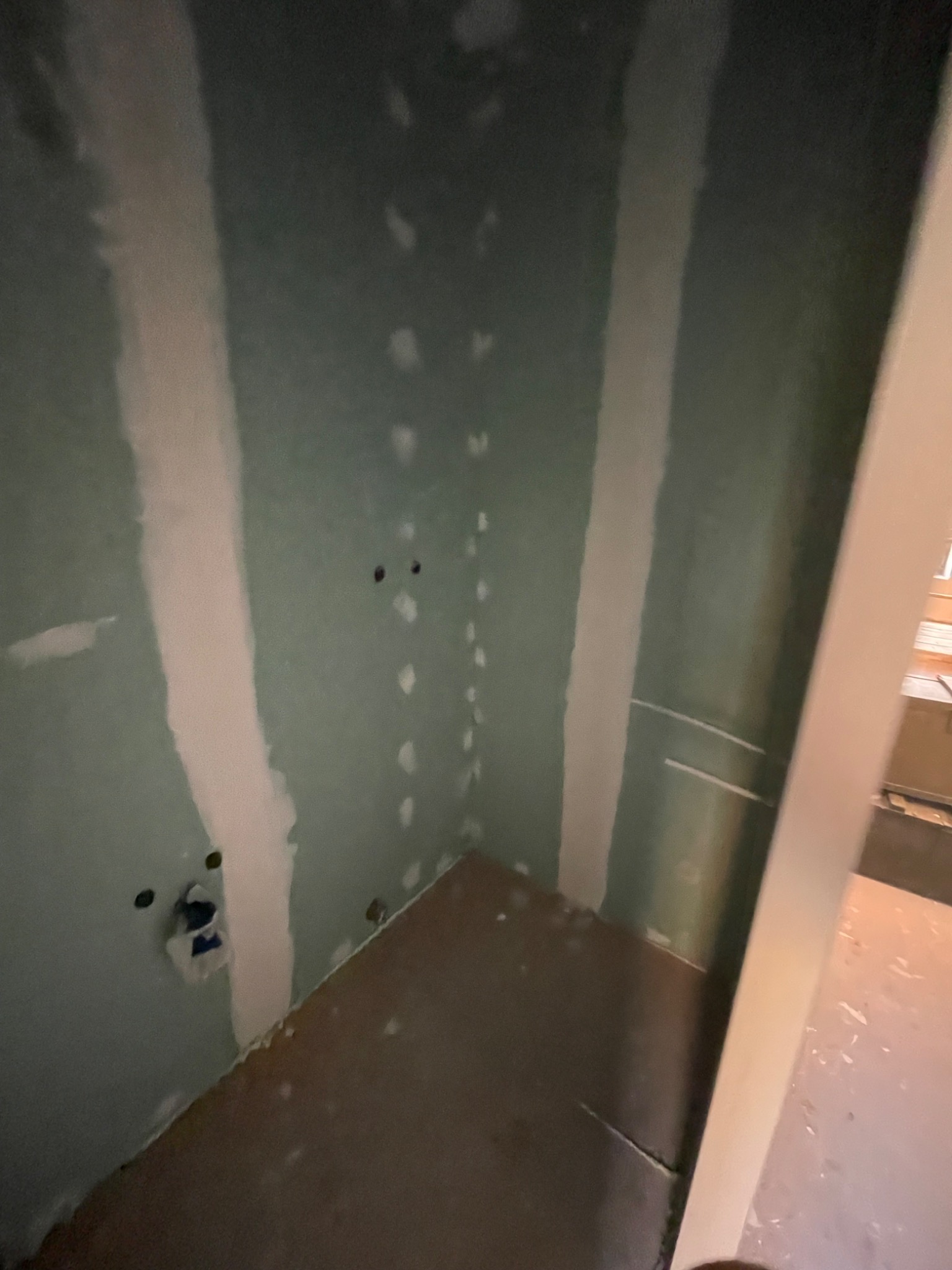 Narożnik pokoju z płytami gipsowo-kartonowymi, widoczne miejsca po szpachlowaniu i przygotowane otwory na instalacje elektryczne, podłoga częściowo zakryta.