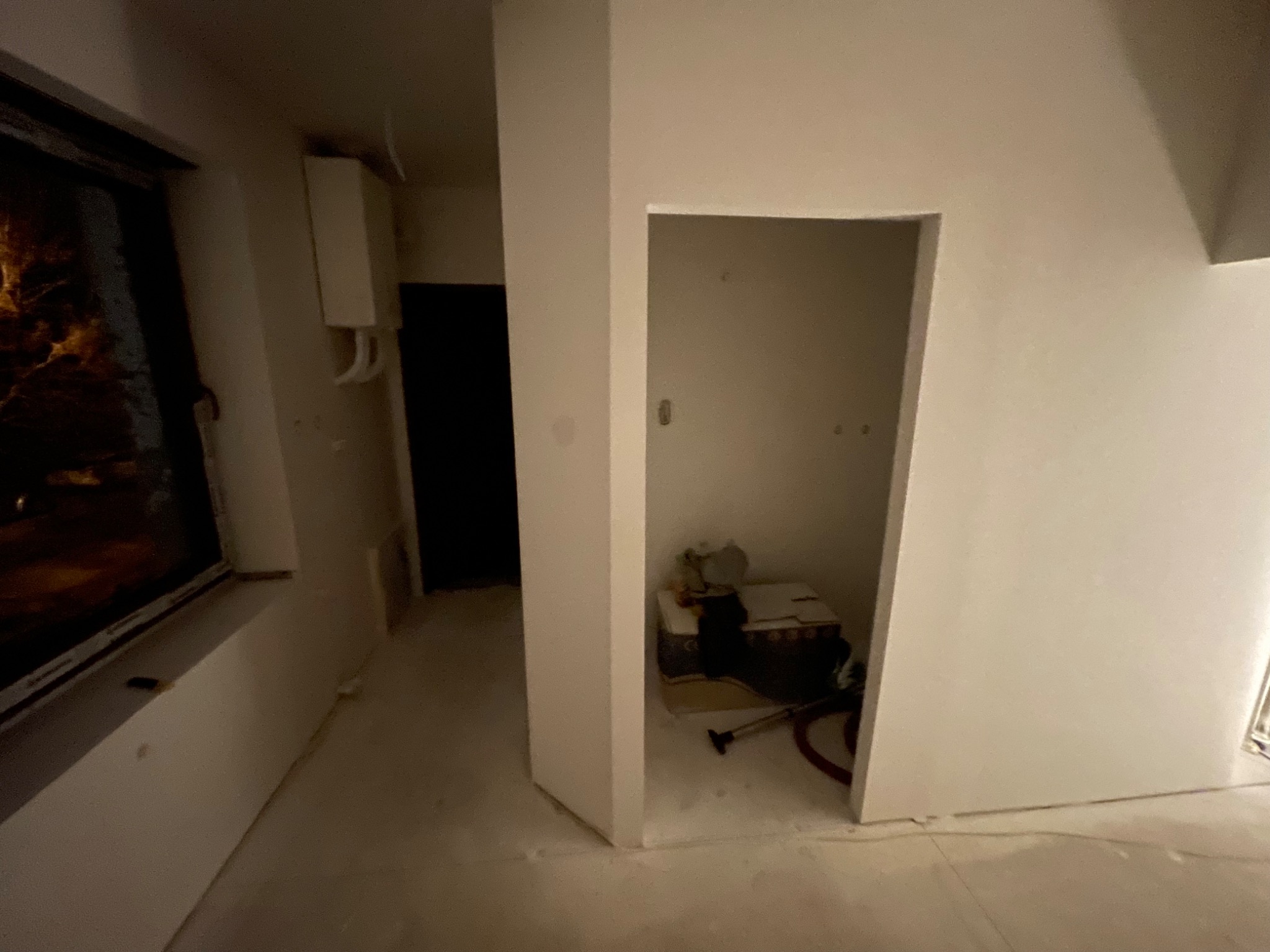 Wnętrze w trakcie prac przygotowawczych, widoczne ściany po szpachlowaniu, przygotowane do dalszych prac wykończeniowych, z widocznym otworem drzwiowym i elementami wyposażenia w głębi.