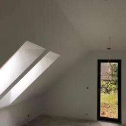 Poddasze z dwoma oknami dachowymi i drzwiami balkonowymi, ściany wstępnie przygotowane pod malowanie, widoczne ślady szpachlowania