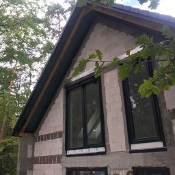 Krawczyk-bud - Budynek w Sochocinie w trakcie budowy elewacji, widoczne bloczki, okna z czarnymi ramami i fragment dachu, otoczenie zielone.
