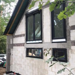 Krawczyk-bud - Surowy stan budynku z betonu komórkowego z zamontowanymi czarnymi oknami, widoczne ślady po zaprawie i przygotowanie do ocieplenia, zieleń w tle.