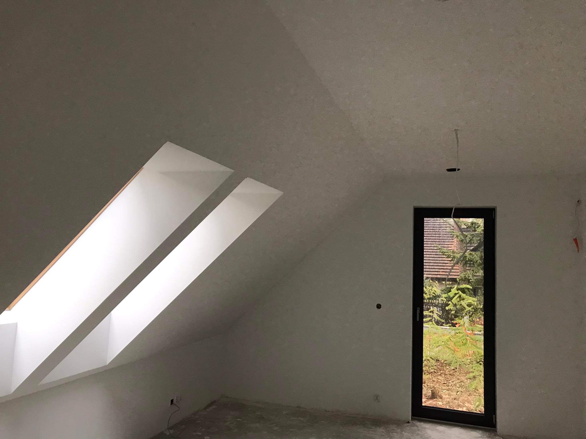 Poddasze z dwoma oknami dachowymi i drzwiami balkonowymi, ściany wstępnie przygotowane pod malowanie, widoczne ślady szpachlowania