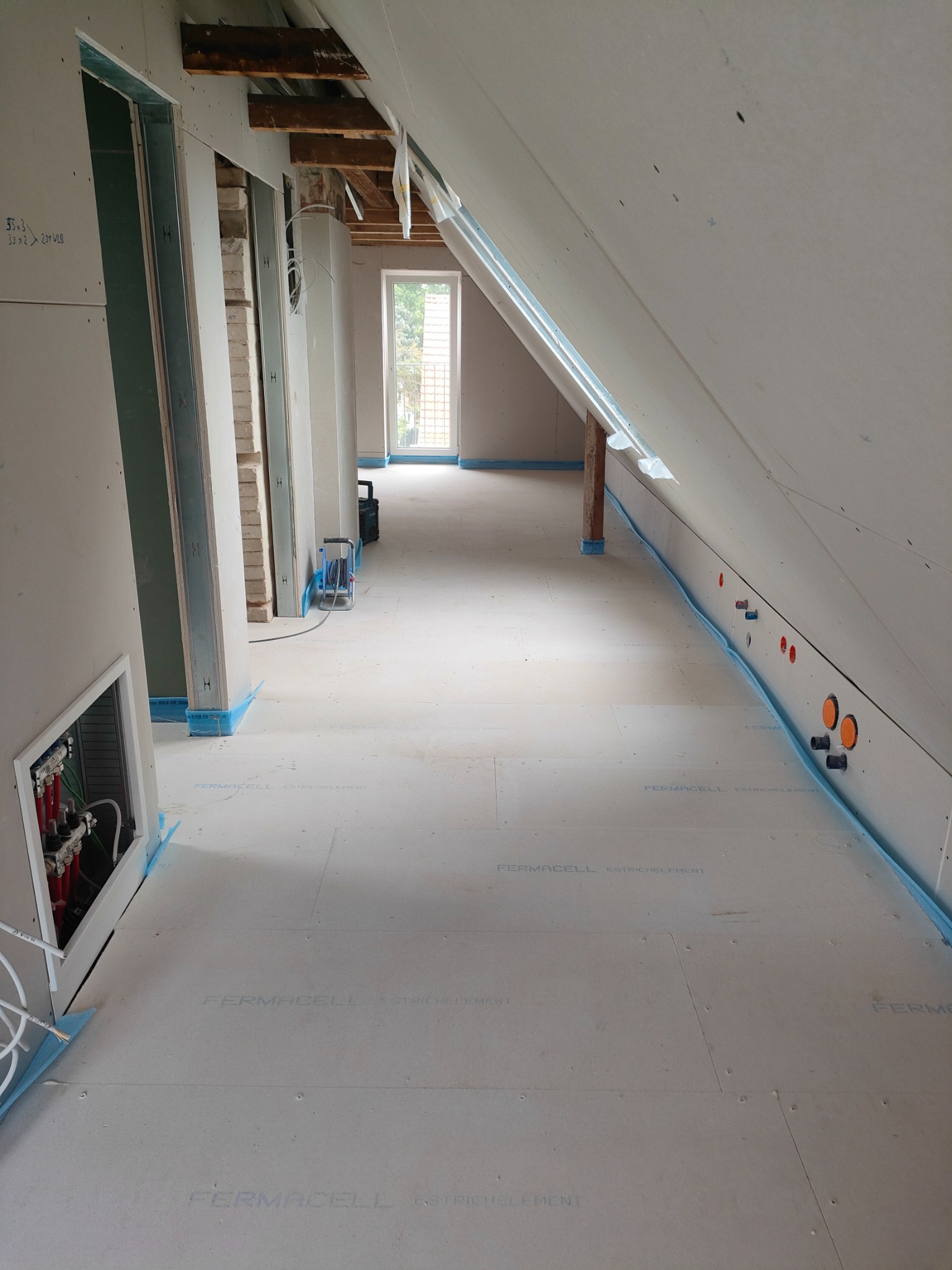 Poddasze w trakcie wykańczania: widoczne płyty Fermacell na podłodze, ściany z płyt karton-gips, instalacje elektryczne i hydrauliczne w ścianach, przygotowane do dalszych prac wykończeniowych.