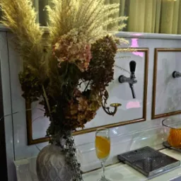 Dekoracja baru z prosecco: wysoki wazon z suszonymi trawami i hortensjami, neonowy napis 'Ti amo prosecco', szklanka prosecco z pomarańczą, biały bar z kranami do nalewania.