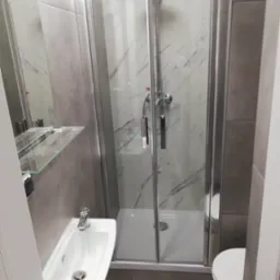 Nowoczesna łazienka z kabiną prysznicową z marmurowymi ścianami, umywalką naścienną i toaletą.