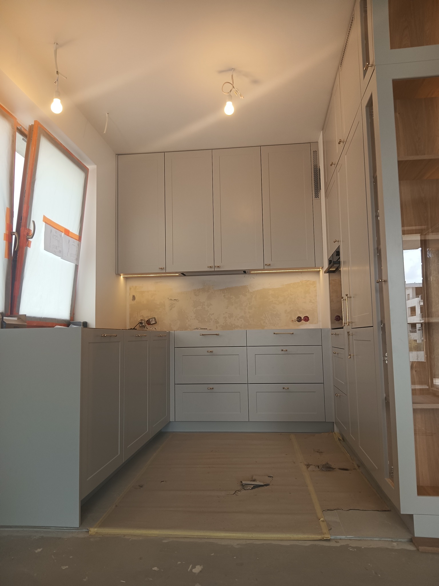 Szara zabudowa kuchenna w trakcie montażu, widoczne niedokończone ściany i zabezpieczona podłoga.