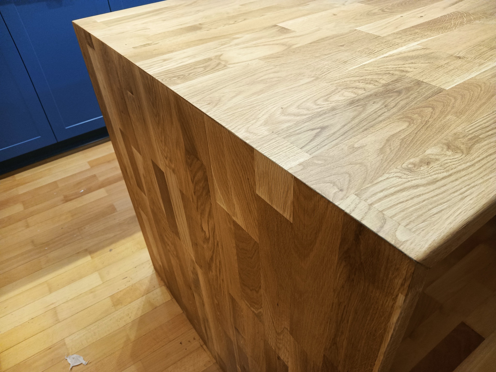 Blat drewniany z widocznymi łączeniami klejonymi, stojący na drewnianej podłodze, obok niebieskiej szafki.