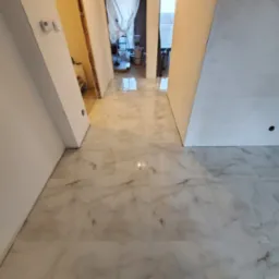 Błyszcząca, marmurowa posadzka w trakcie remontu, z widocznymi fragmentami ścian przygotowanych do malowania i odsłoniętą konstrukcją drzwiową w tle.